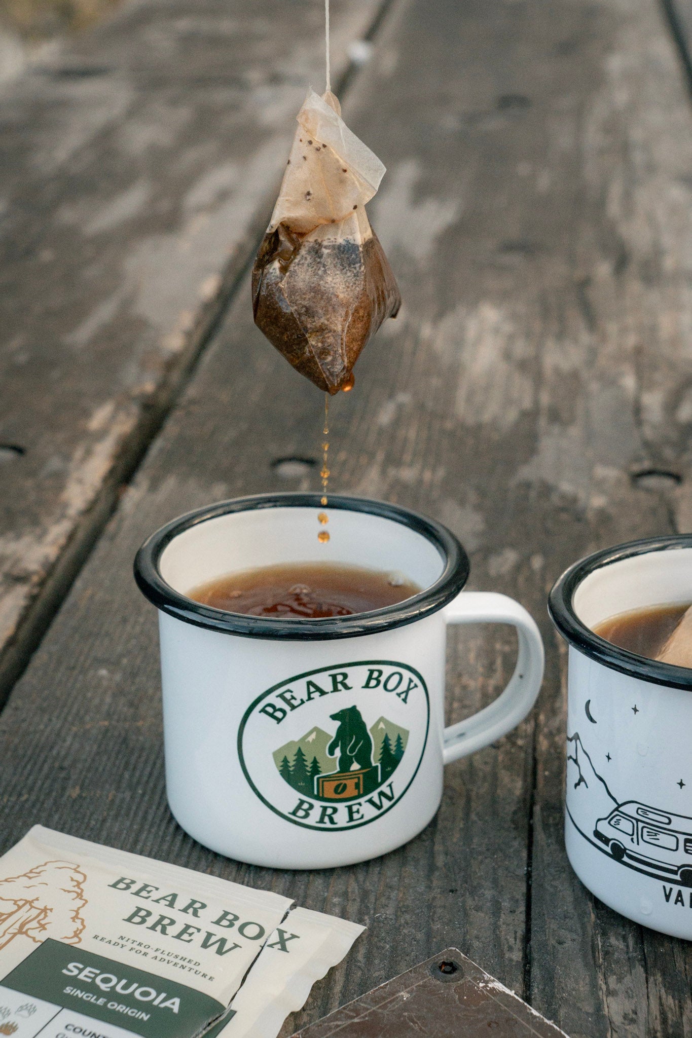 Coffee bag being dripped into a 'Bear Box Brew' mug on a wooden surface.