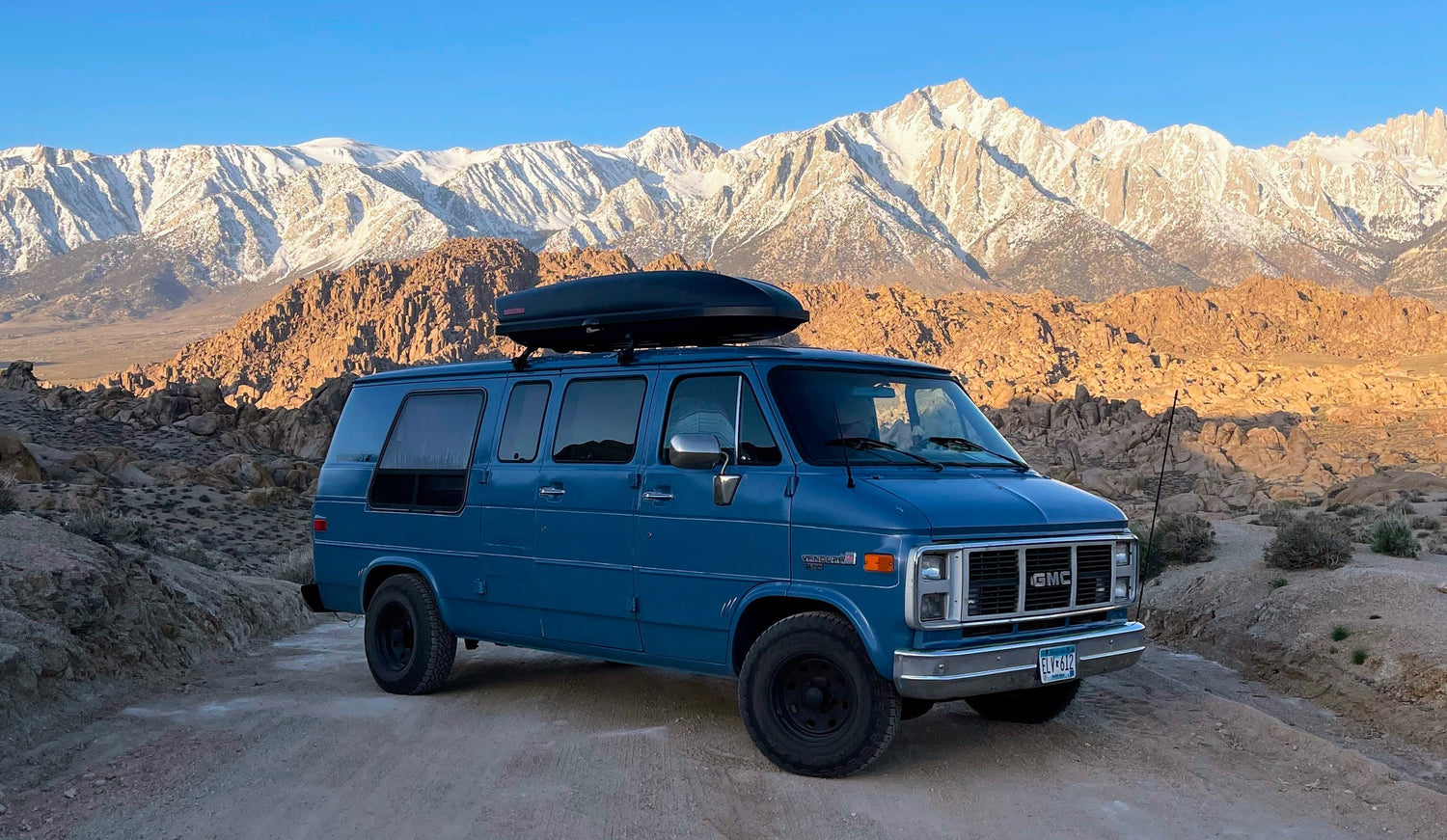 A vintage blue camper van on Movie Road at Alabama Hills in California with the Sierra Nevada mountain range in the background.